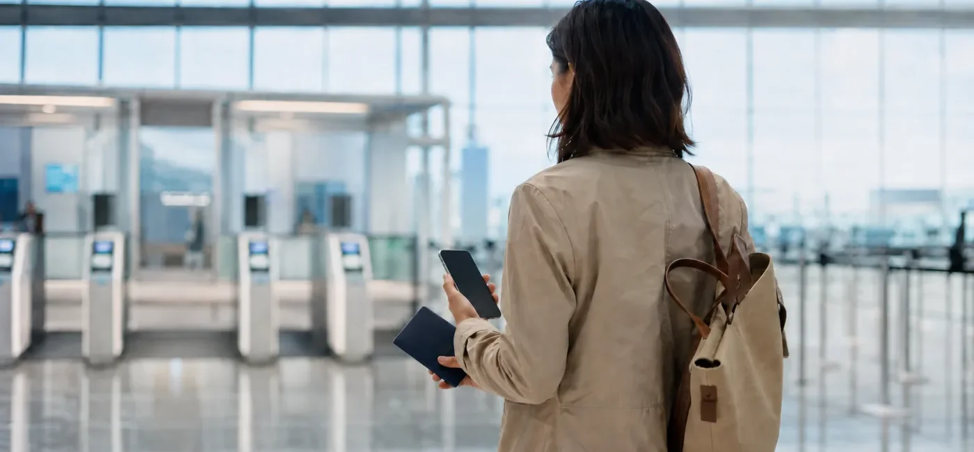 Traveler carrying a physical passport and phone toward Mobile Passport Control inspection in a U.S. airport