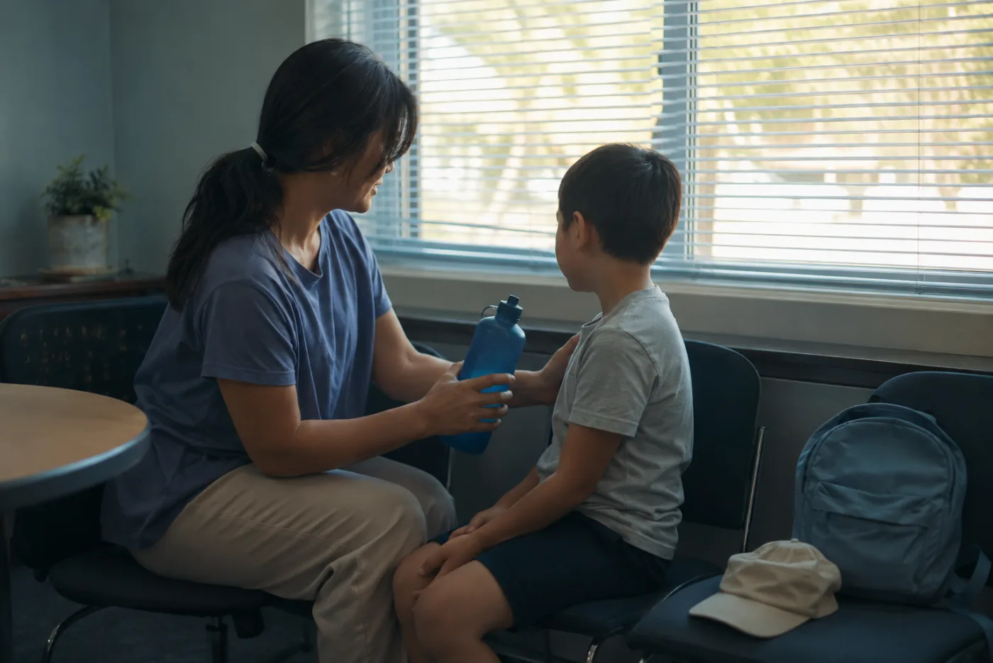A caregiver giving a child water and checking for heat symptoms in a cool shaded room after early dismissal